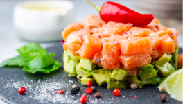 Délicieuse salade d'avocat et de saumon cru, tartare, servie sur une plaque noire au citron vert, fond clair