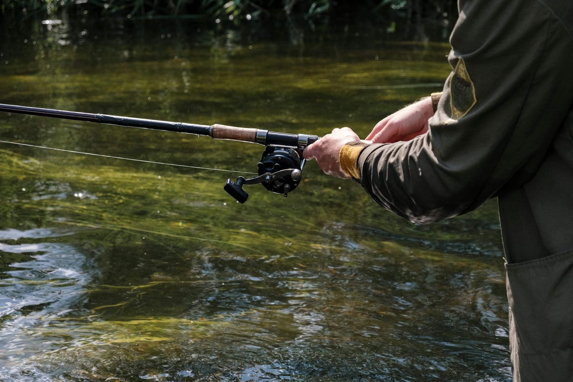 Gros plan sur les mains d'un pécheur tenant sa canne à moulinet pendant une partie de pêche en rivière.