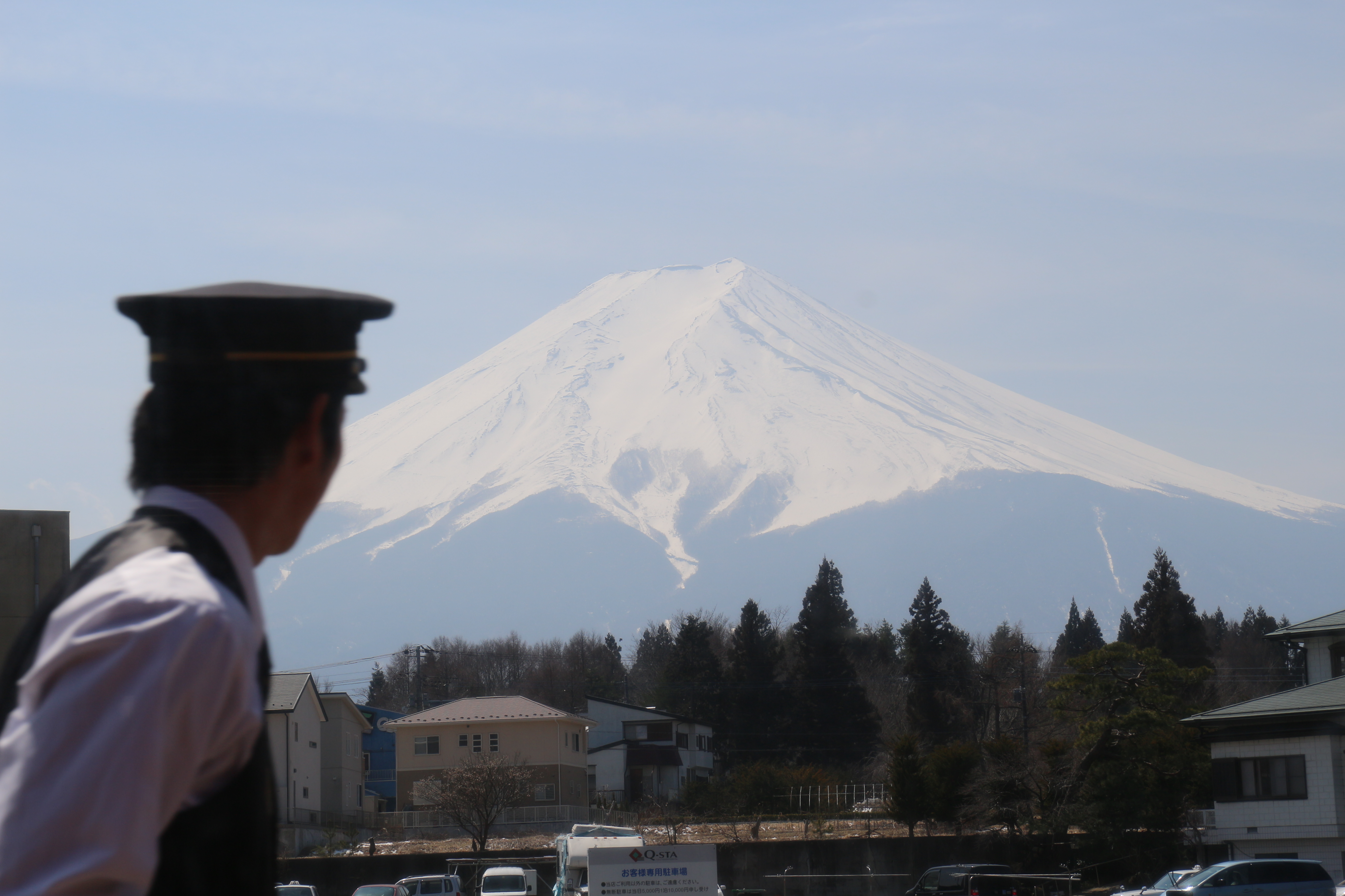 Une photo du mont Fuji. Au premier plan, un peu flouté, un employé de la gare en uniforme regarde en direction de la montagne.